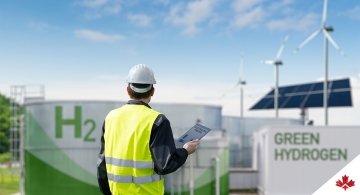 Engineer with a tablet in front of a hydrogen factory with blue, sunny skies.