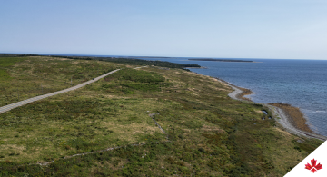 Aerial view showing a green landscape split by a freeway and the ocean to the right-hand side.