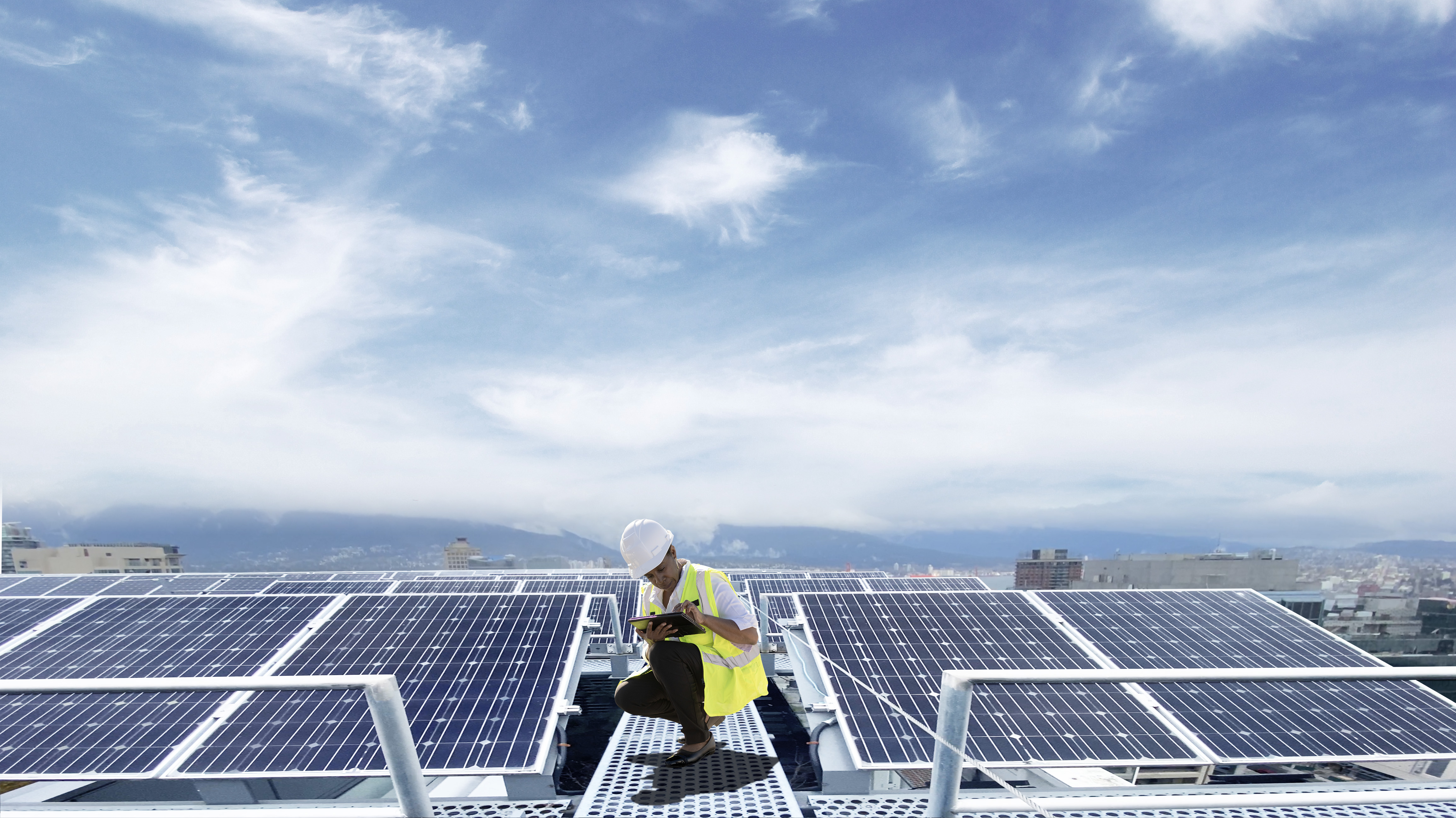 Woman in hard hat and vest working on a tablet amongst industrial solar panels in Canada