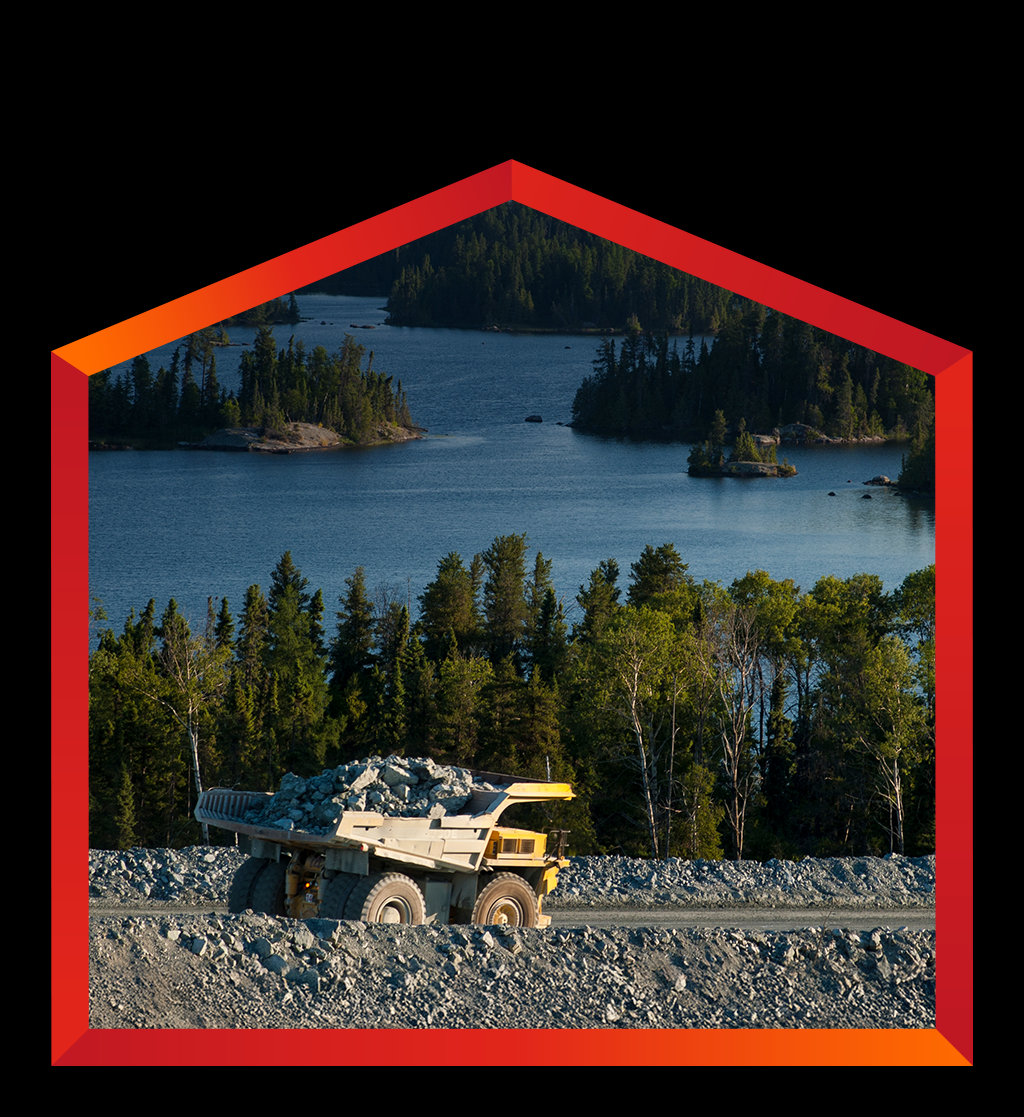 A large, yellow and grey mining dump truck, heavily loaded with rocks, drives on a dirt road in Canada.