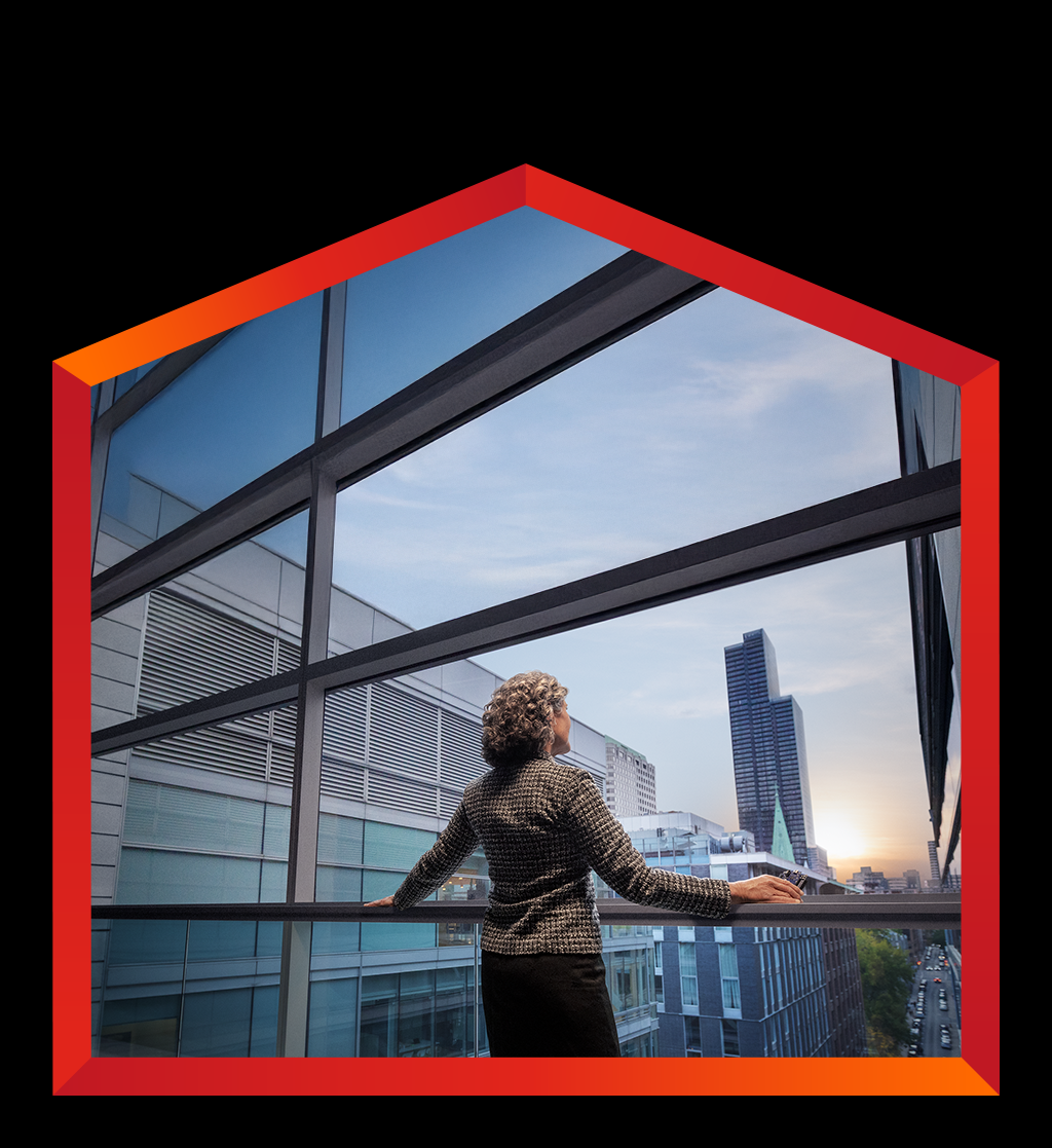 A female is seen from behind, standing and looking out a large, floor-to-ceiling window or balcony. The person is wearing a dark, professional-looking jacket, with their hands resting on a dark horizontal railing. Beyond the window, a modern cityscape is visible with multiple tall, glass-fronted buildings in Canada.