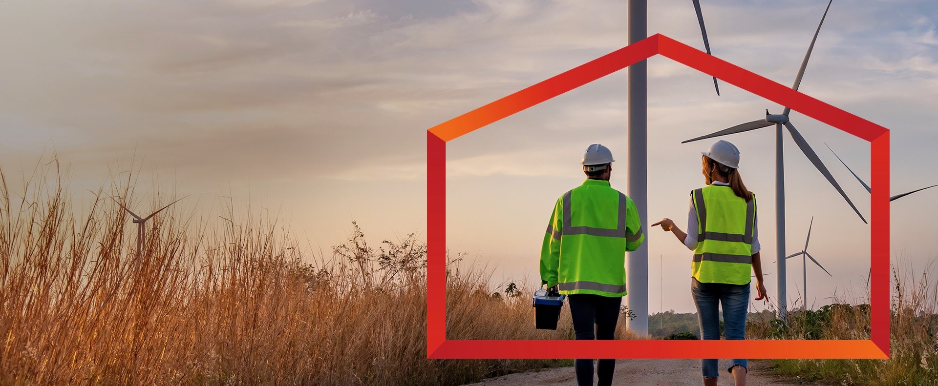 Two individuals, seen from behind, walk down a dirt road towards several wind turbines in the distance. Both wear safety vests (one green, one yellow) and hard hats, suggesting they are inspecting a wind farm in Canada.