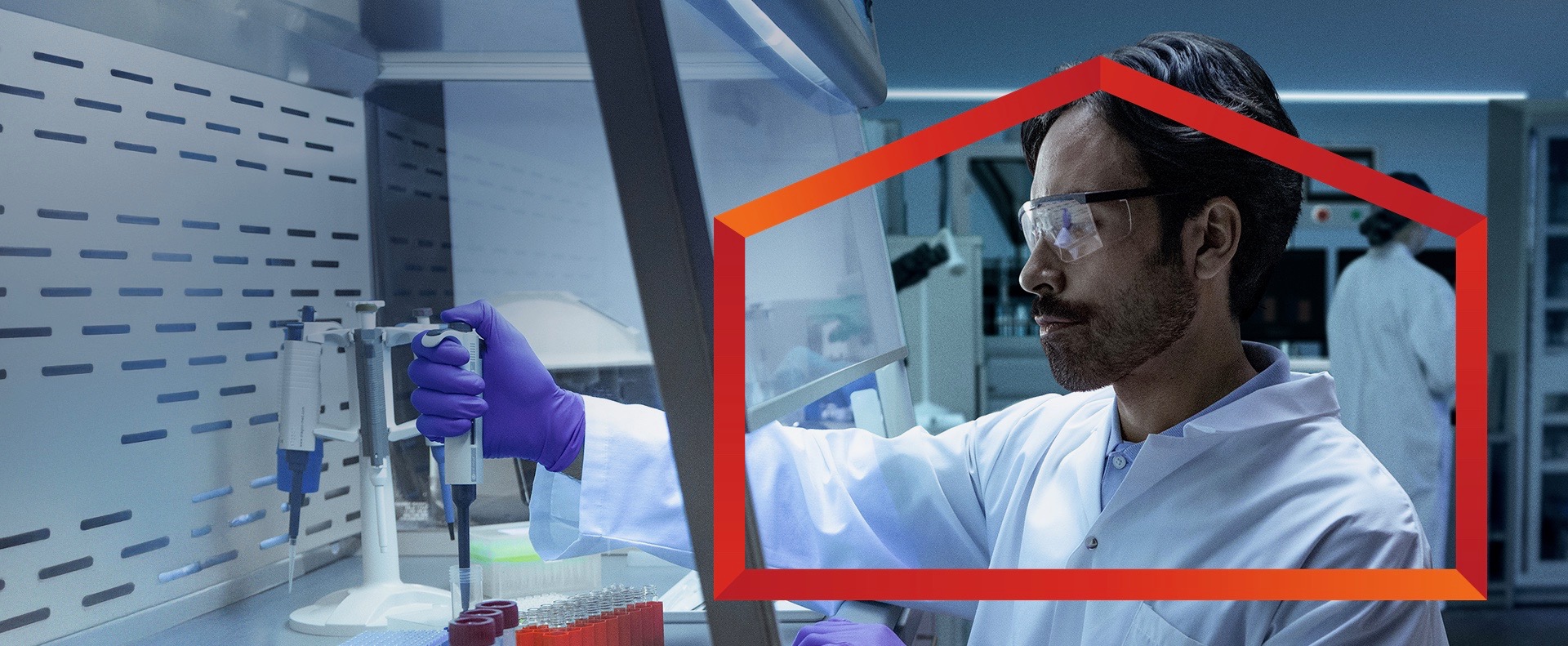 A male scientist in a white lab coat, purple gloves, and safety glasses works inside a fume hood, carefully pipetting liquid into a small beaker in Canada. 